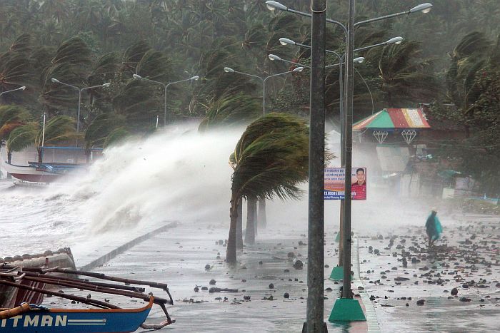 A resident (R) walks past high waves pounding the sea wall amidst strong winds as Typhoon Haiyan hit the city of Legaspi, Albay province, south of Manila on November 8, 2013. One of the most intense typhoons on record whipped the Philippines on November 8, killing three people and terrifying millions as monster winds tore roofs off buildings and giant waves washed away flimsy homes.AFP PHOTO/CHARISM SAYAT
