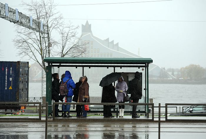 Cilvēki sabiedriskā transporta pieturvietā lietus un krusas laikā pilsētā.
