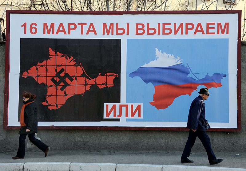People walk past a poster in Sevastopol on March 11, 2014 reading “On March 16 we will choose either… or…”, depicting Crimea in red with a swastika and covered in barbed wire (L) and Crimea with the colors of the Russian flag. Pro-Moscow lawmakers in Crimea voted for independence from Ukraine on March 11 in a precursor to a referendum this weekend for the region to become part of Russia. AFP PHOTO/ VIKTOR DRACHEV