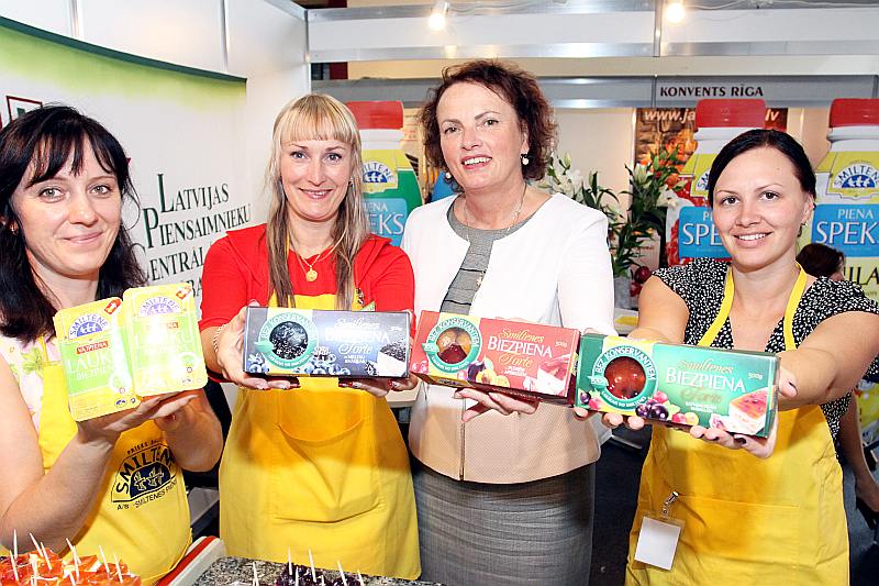 AS “Smiltenes piens” padomes priekšsēdētāja Gita Mūrniece kopā ar uzņēmuma darbiniecēm kādā~no “Rīga Food” izstādēm, demonstrējot biezpiena tortes.