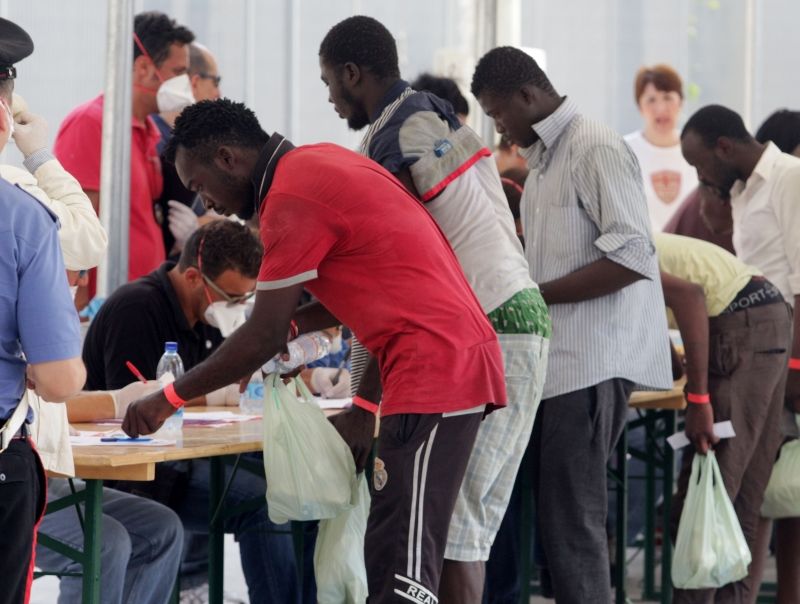 Migranti aizpilda identifikācijas dokumentus Palermo ostā Itālijā.