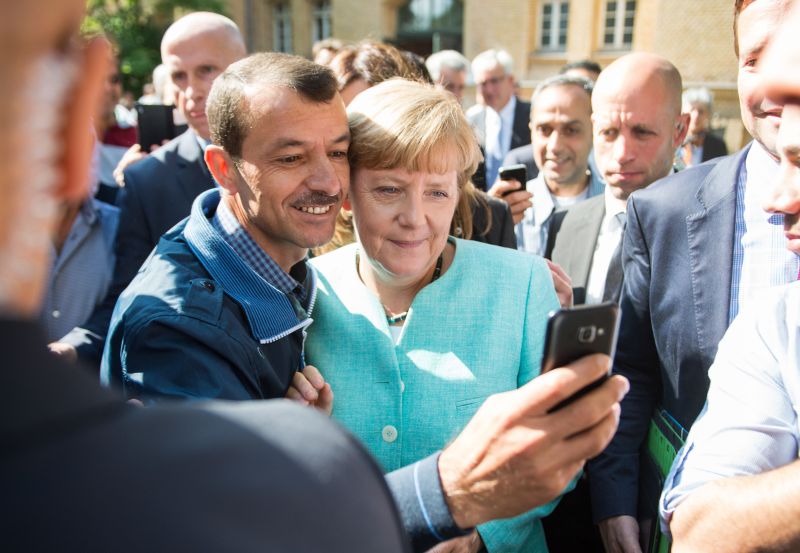 Asylum seeker (C, L) takes a selfie picture with German Chancellor Angela Merkel (C, R) following Merkel’s visit at a branch of the Federal Office for Migration and Refugees and a camp for asylum-seekers in Berlin on September 10, 2015. Around 450,000 refugees have arrived in Germany so far this year, including 37,000 in the first eight days of September, Vice Chancellor Sigmar Gabriel told parliament on Thursday. Chancellor Angela Merkel has urged the 28-nation bloc to go further and agree on a proportional distribution of refugees with no limits on actual numbers, amid a record influx from war-torn Syria and other countries.