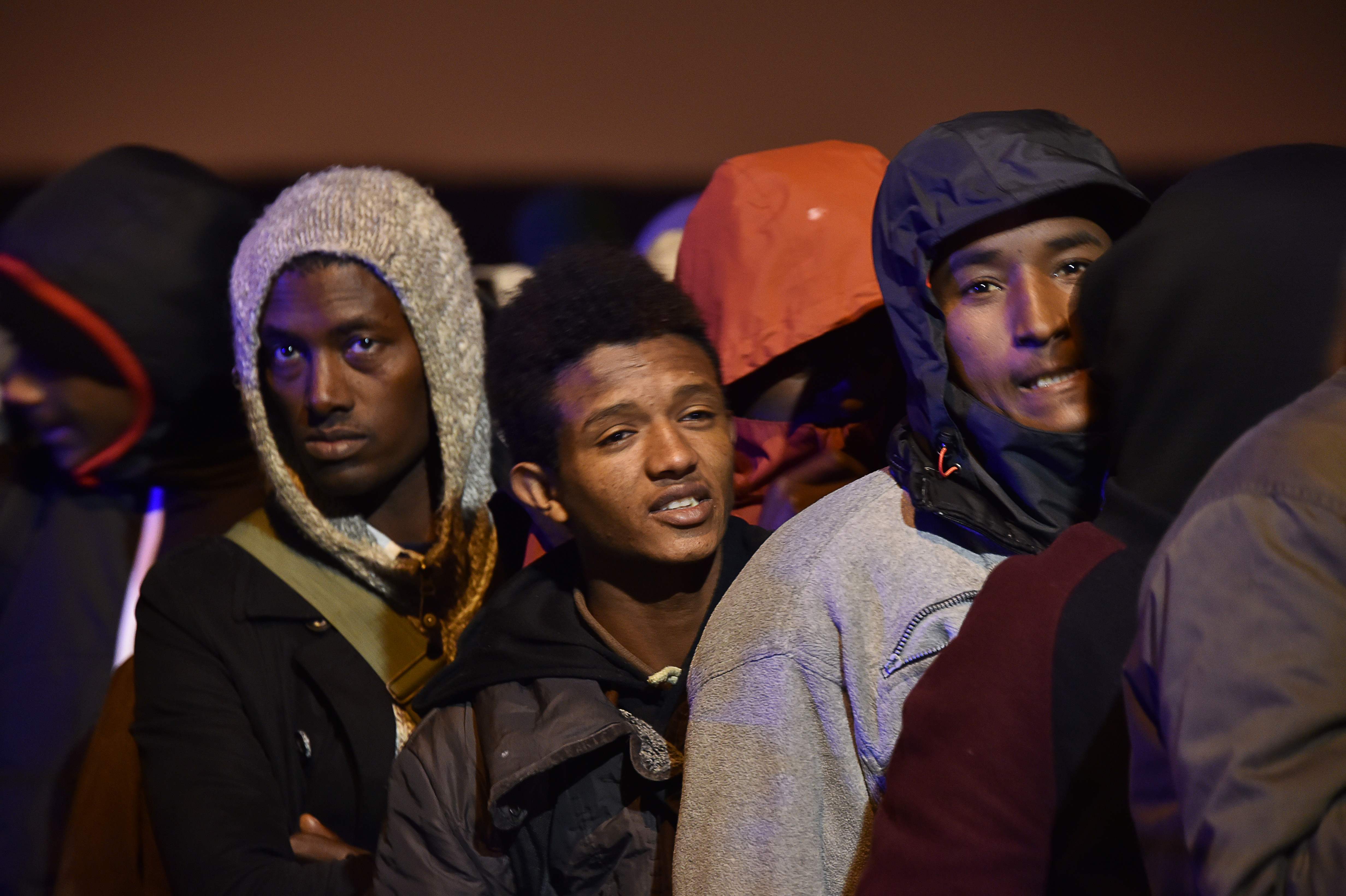 Migranti ar savām personiskajām mantām sākuši pulcēties pie noliktavas, kas kalpo par centrālo punktu nometnes evakuācijas operācijā.