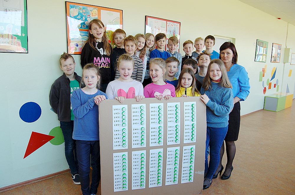 Zvejniekciema vidusskolas 3. klases skolēni un klases audzinātāja Jolanta Liniņa (no labās) izrāda savu “labo darbu” – reizrēķina tabulu, kas tapusi no 100 vienādiem PET pudeļu korķīšiem.