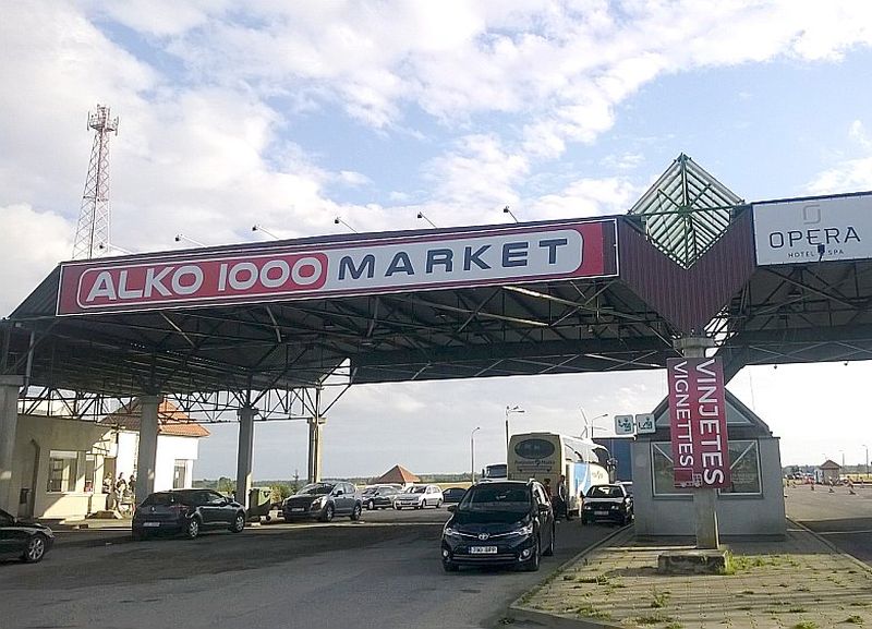 Reklāma, kas piestiprināta pie jumta malas virs bijušā robežpunkta būdiņām, vēsta, ka tūristi ieradušies valstī “ALKO 1000 MARKET”, nevis Latvijā.