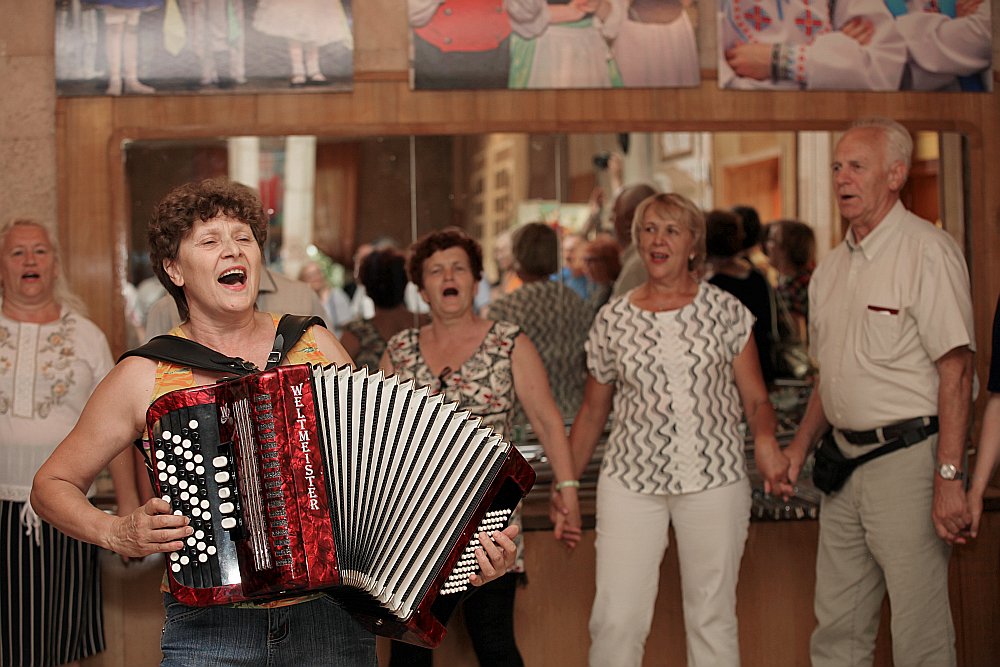 Omskas Latviešu biedrības ļaudis ciemiņus sagaidīja ar dziesmu “Šeit ir Latvija”. Priekšplānā folkloras ansambļa “Daina” vadītāja Raja Bakanova.