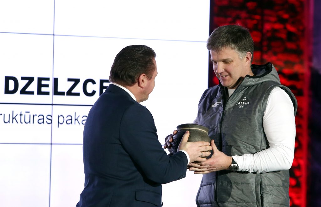 VAS “Latvijas dzelzceļš” prezidents Edvīns Bērziņš dāvina bobsleja izlases galvenajam trenerim Sandim Prūsim meduspodu Latvijas Olimpiskās komandas “Phjončhana 2018” prezentācijas pasākumā Latvijas Dzelzceļa vēstures muzejā.