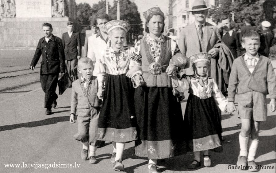 1948. gada 21. jūlijs. Ģimene nāk no dziesmu svētkiem Esplanādē. Fotogrāfijas centrā Frīda Puzule, kura darinājusi tautas tērpu ne tikai sev, bet arī saviem bērniem un radu bērniem. No kreisās: Jānis Pladers, Inta Kalniņa, Frīda Puzule, Ieva Puzule, Andris Puzulis.