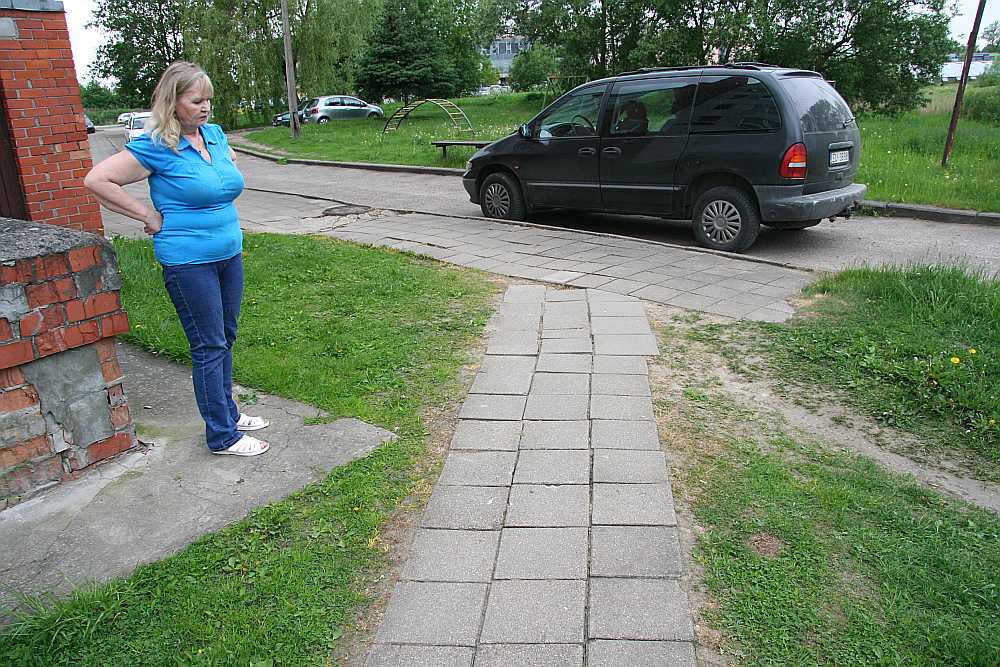 Mājas vecākā Raisa Dubeņecka uz mājas sabojātās aizsargplāksnes pie gājēju celiņa, kas jau sakārtots.