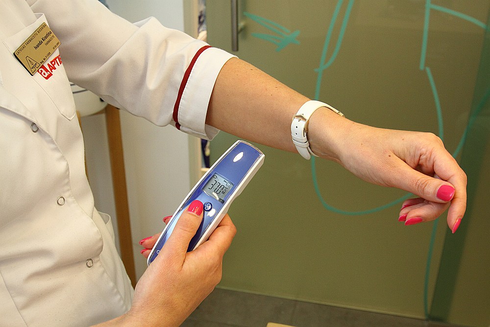 Farmaceite Ivanda Krastiņa rāda digitālo bezkontaktu termometru.
