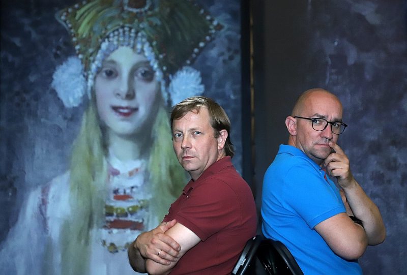 Renārs Sproģis (no labās) kopā ar līdzproducentu Ivo Valdovski Cēsu Pilsmuižas klētī izveidojis neparastu multimediju izstādi “Simbolisms”, kas jaunās krāsās, skaņās un kustībā atklāj vairāk nekā 40 spilgtākos latviešu vecmeistaru darbus. Attēla fonā: Jaņa Rozentāla glezna “Laila kokošņikā”. 1913. g. Privātkolekcija.